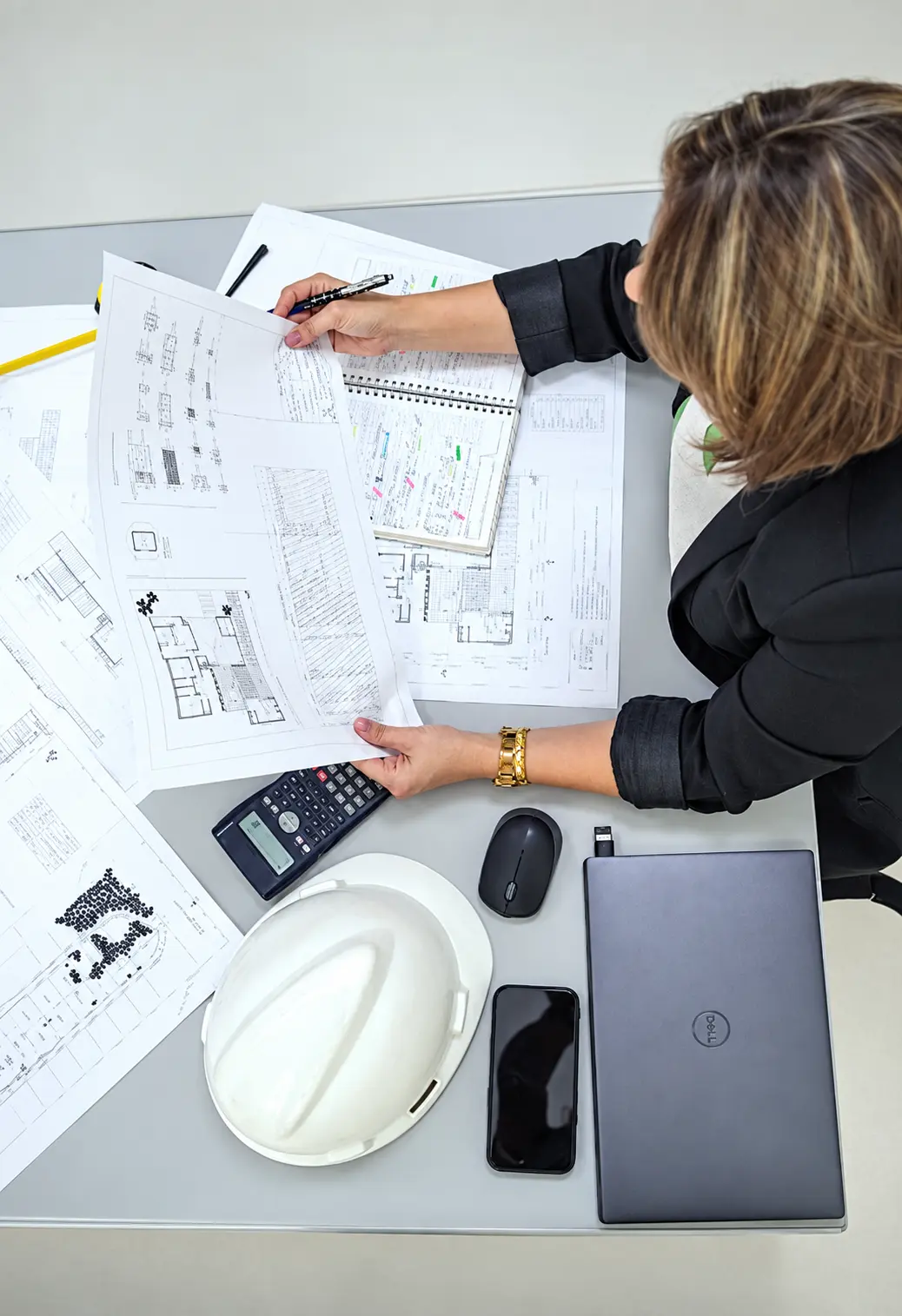 Engenheira analisando pranchas de projeto e planilha de orçamento na mesa de trabalho